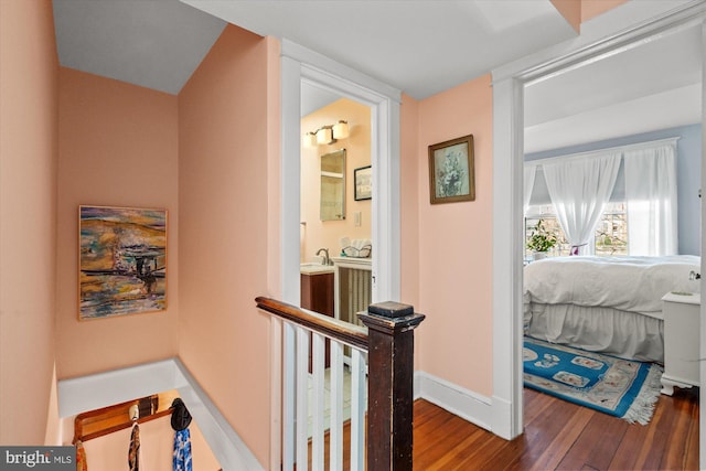 corridor with an upstairs landing, wood finished floors, and baseboards