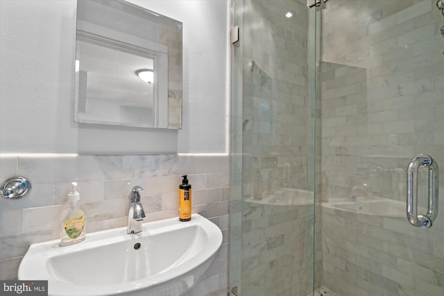 bathroom with a sink, a wainscoted wall, tile walls, and a shower stall