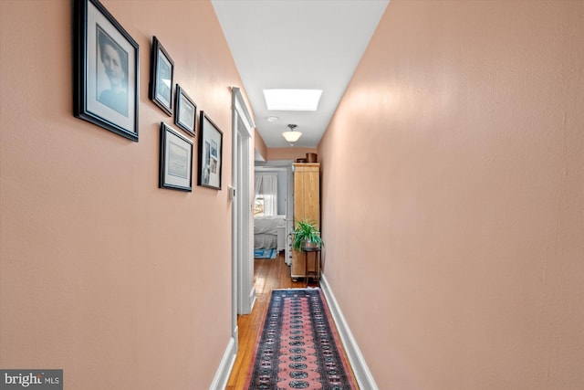 corridor with baseboards, a skylight, and light wood-style floors