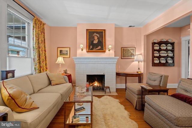 living area featuring visible vents, a brick fireplace, baseboards, and wood finished floors