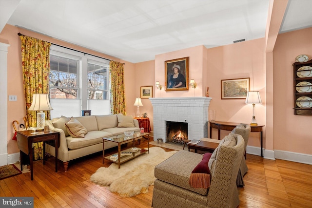 living room with visible vents, a brick fireplace, baseboards, and hardwood / wood-style flooring