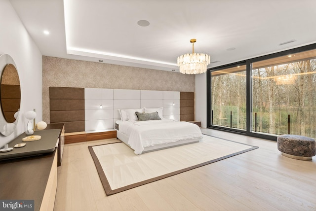 bedroom with visible vents, an accent wall, floor to ceiling windows, wood finished floors, and a notable chandelier