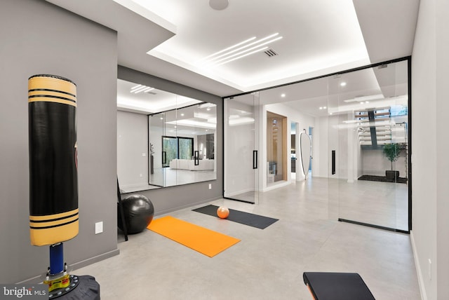 workout room with visible vents, a raised ceiling, and baseboards