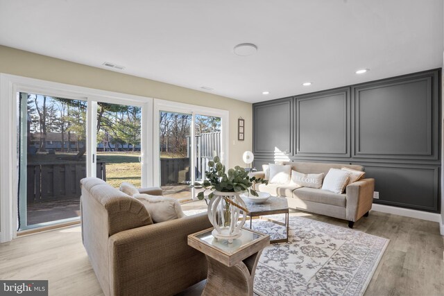 living area with recessed lighting, visible vents, light wood-style flooring, and a decorative wall