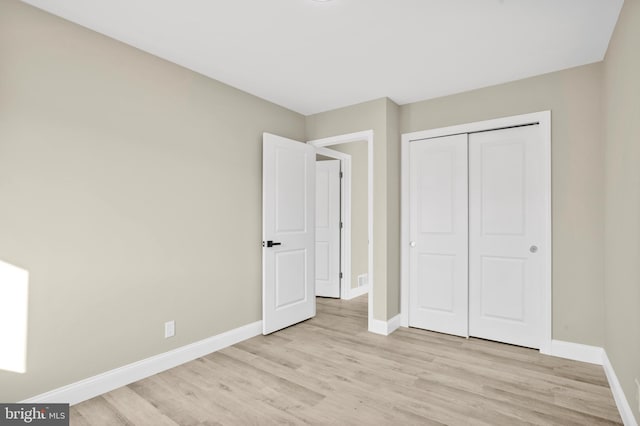 unfurnished bedroom with light wood-style flooring, baseboards, and a closet