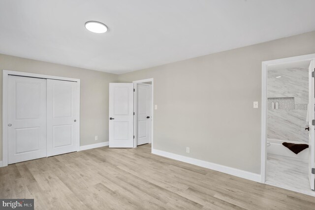 unfurnished bedroom with a closet, baseboards, connected bathroom, and light wood finished floors