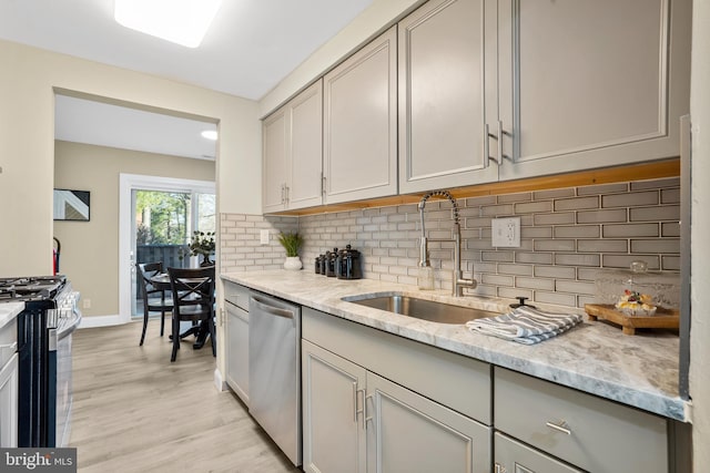 kitchen featuring a sink, gray cabinetry, stainless steel appliances, light wood-style floors, and tasteful backsplash