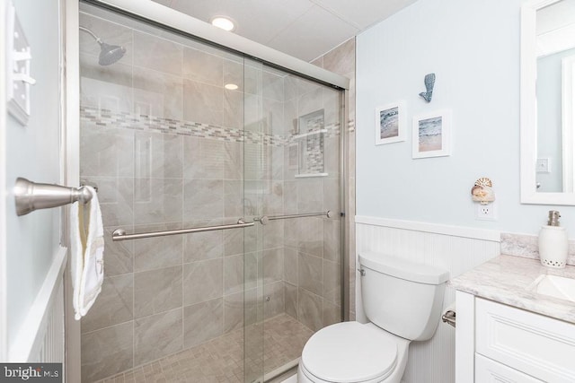 bathroom featuring vanity, toilet, a stall shower, and wainscoting