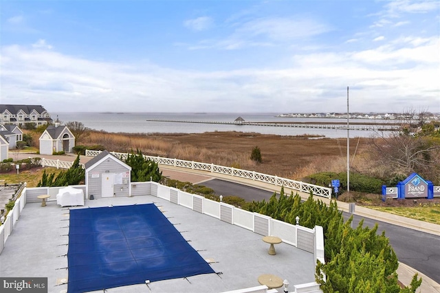 community pool with fence, a patio, and a water view