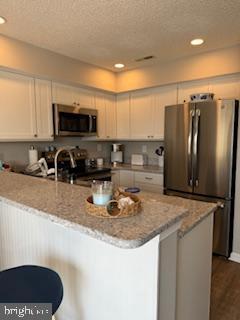 kitchen with light stone counters, a textured ceiling, appliances with stainless steel finishes, and a peninsula