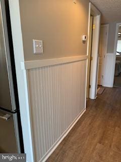 corridor with a wainscoted wall, a textured ceiling, and wood finished floors