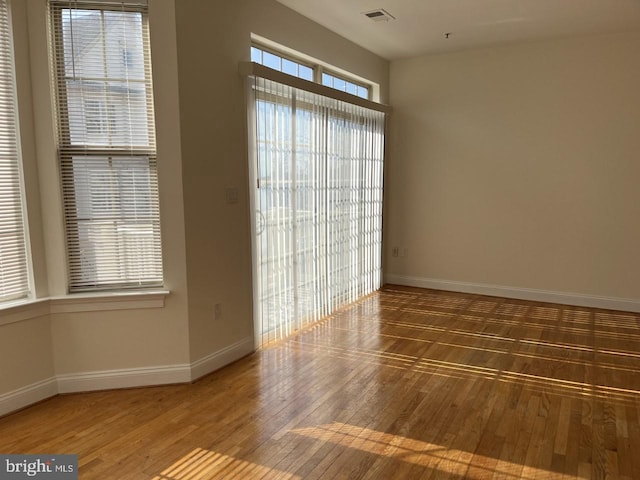 unfurnished room with a healthy amount of sunlight, visible vents, and wood-type flooring