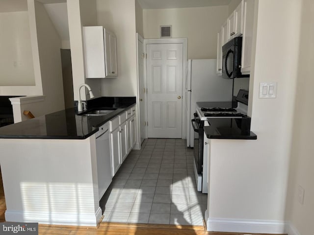 kitchen with a peninsula, a sink, black appliances, white cabinets, and dark countertops