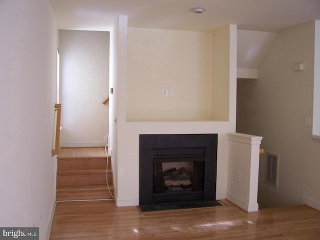 unfurnished living room with visible vents, stairs, a fireplace with flush hearth, and wood finished floors