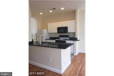 kitchen with a sink, stove, white cabinets, black microwave, and dark countertops