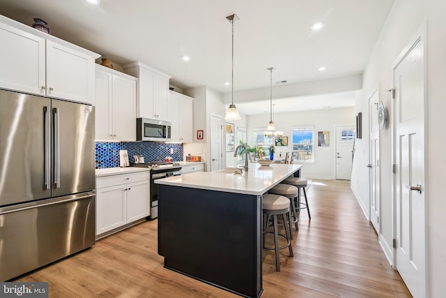 kitchen with a breakfast bar, a sink, stainless steel appliances, light wood finished floors, and decorative backsplash