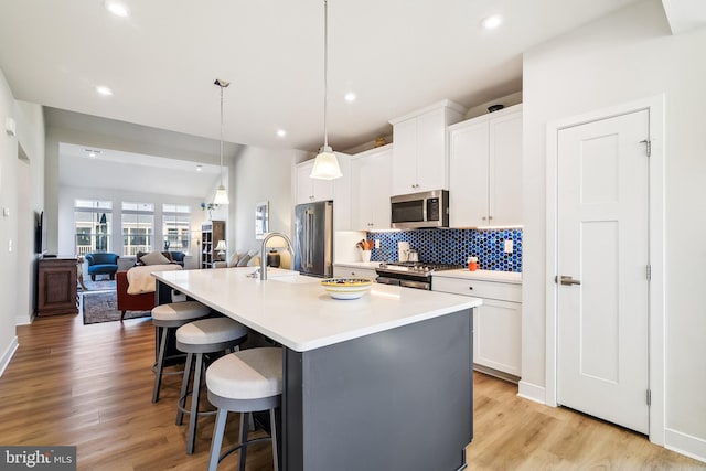 kitchen featuring an island with sink, a sink, stainless steel appliances, a kitchen breakfast bar, and tasteful backsplash