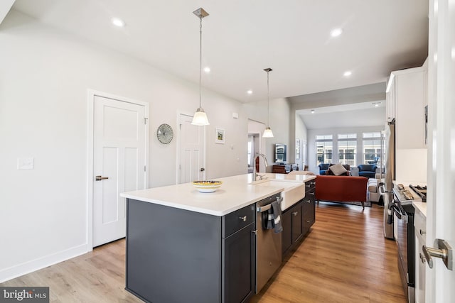 kitchen with an island with sink, stainless steel appliances, a sink, light countertops, and light wood-type flooring