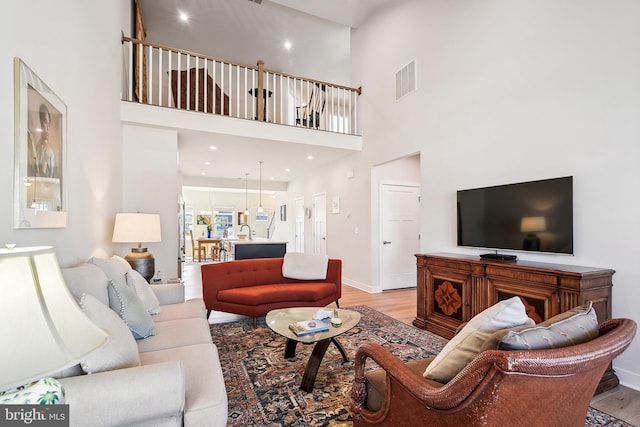 living room with baseboards, visible vents, a high ceiling, light wood-style flooring, and recessed lighting