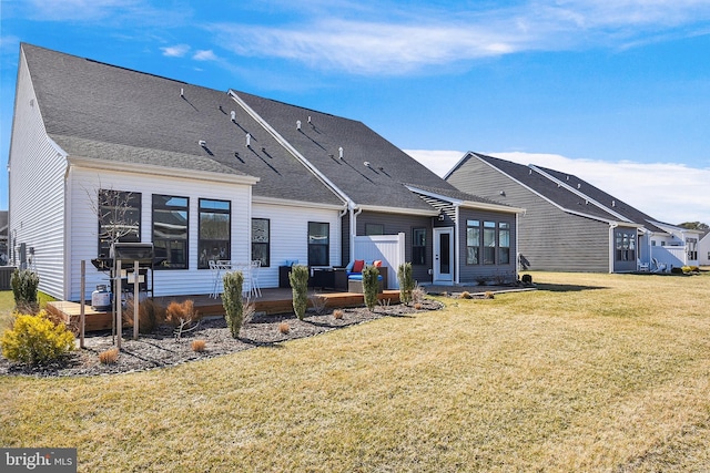 back of house featuring a wooden deck, a lawn, and a shingled roof