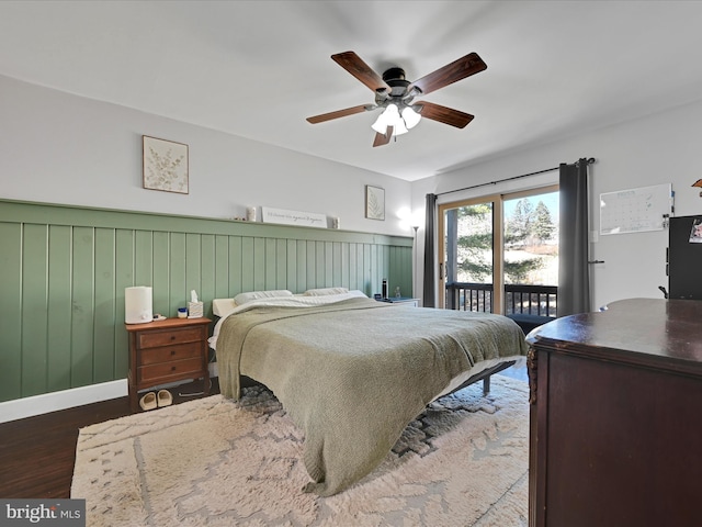 bedroom with wainscoting, wood finished floors, a ceiling fan, and access to outside