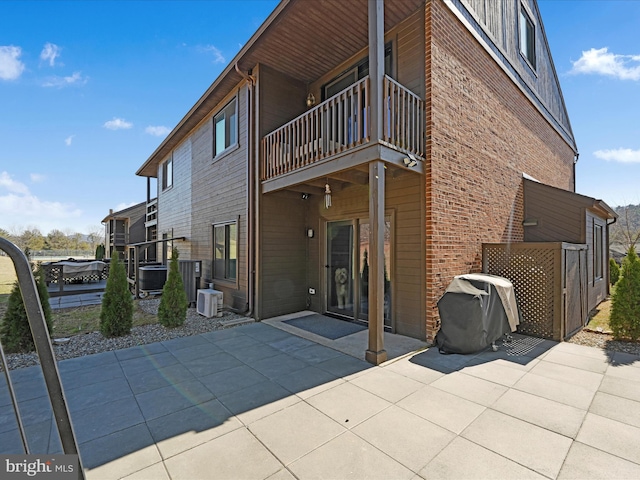 rear view of property featuring a balcony, cooling unit, a patio area, and brick siding