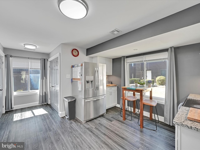 kitchen with visible vents, baseboards, white cabinets, wood finished floors, and stainless steel fridge