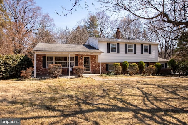 split level home featuring brick siding, a porch, a chimney, and a front yard