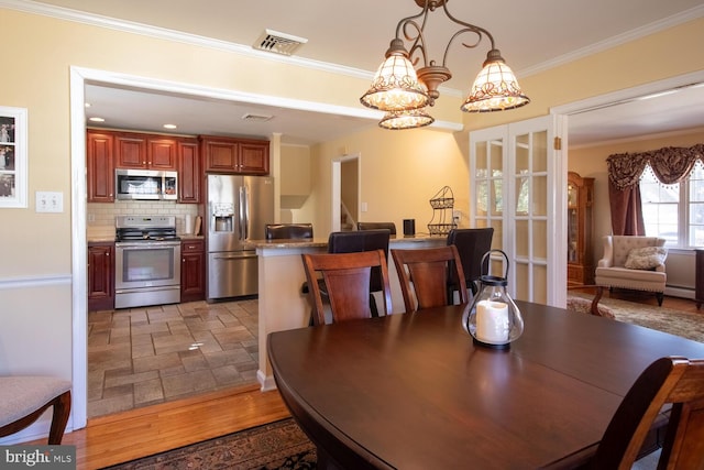 dining area with visible vents, a notable chandelier, ornamental molding, a baseboard heating unit, and stone finish flooring