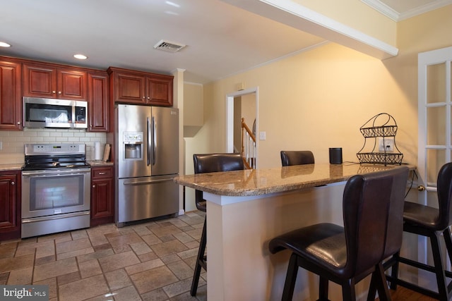 kitchen featuring visible vents, ornamental molding, tasteful backsplash, appliances with stainless steel finishes, and a breakfast bar area