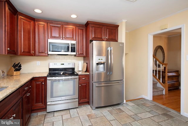 kitchen with baseboards, ornamental molding, stone tile floors, decorative backsplash, and stainless steel appliances