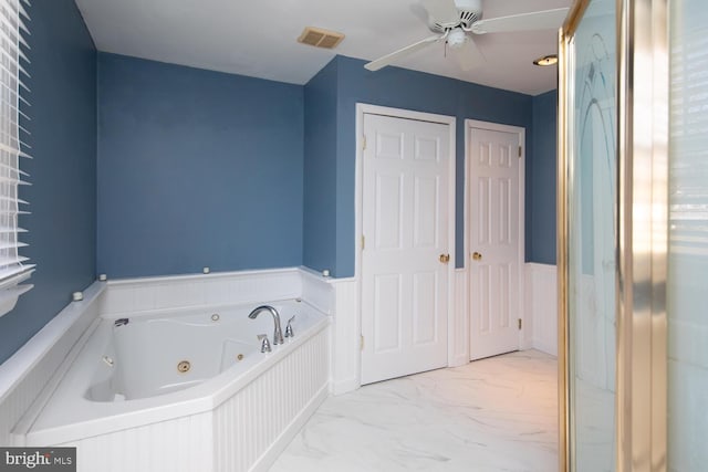 bathroom with a tub with jets, marble finish floor, a ceiling fan, and a wainscoted wall