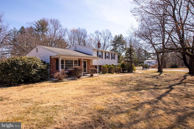 view of front of house featuring brick siding, a chimney, and a front yard