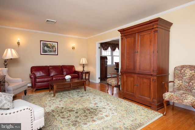 living area featuring baseboards, visible vents, a baseboard radiator, ornamental molding, and light wood-type flooring