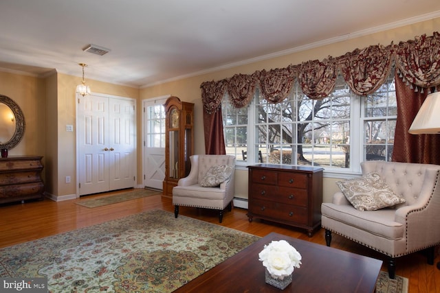 living area with visible vents, wood finished floors, ornamental molding, and a baseboard radiator