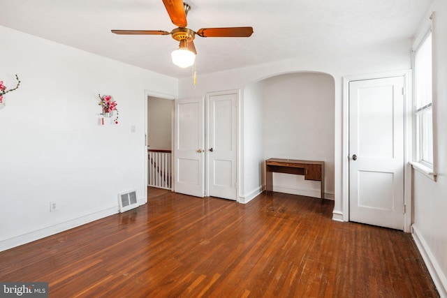 unfurnished bedroom featuring baseboards, visible vents, arched walkways, ceiling fan, and wood-type flooring