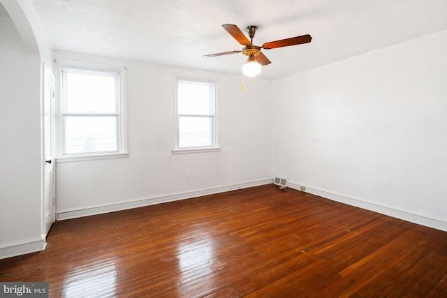 unfurnished room with arched walkways, a ceiling fan, baseboards, and wood-type flooring