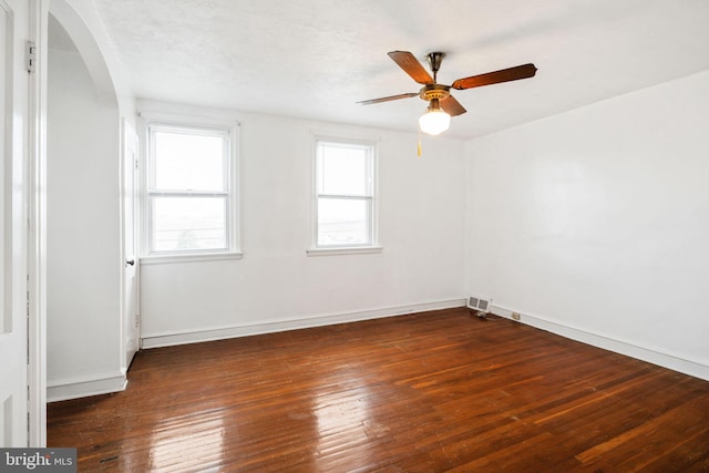 empty room featuring arched walkways, visible vents, baseboards, and hardwood / wood-style floors