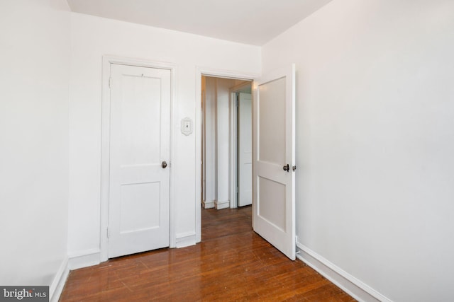 empty room with baseboards and dark wood-type flooring