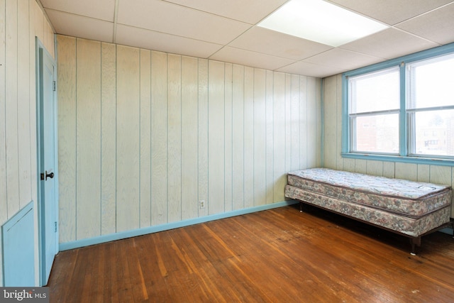 unfurnished bedroom featuring baseboards, a paneled ceiling, hardwood / wood-style floors, and wood walls