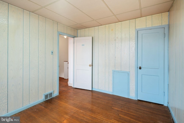 unfurnished bedroom with visible vents, a drop ceiling, wood walls, and wood finished floors