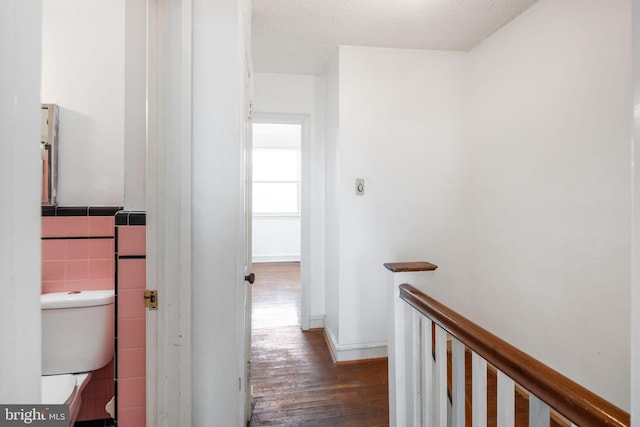 corridor featuring an upstairs landing, a textured ceiling, tile walls, and hardwood / wood-style flooring