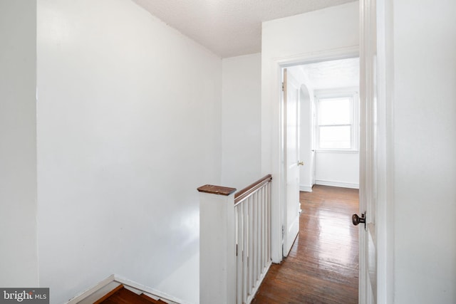 hall with baseboards, an upstairs landing, a textured ceiling, and dark wood-style flooring