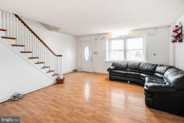 unfurnished living room featuring visible vents, baseboards, stairway, light wood-type flooring, and a textured ceiling