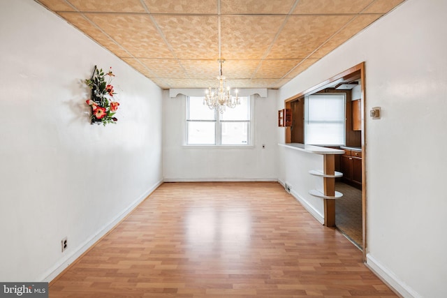 unfurnished dining area with a notable chandelier, light wood-style floors, and baseboards