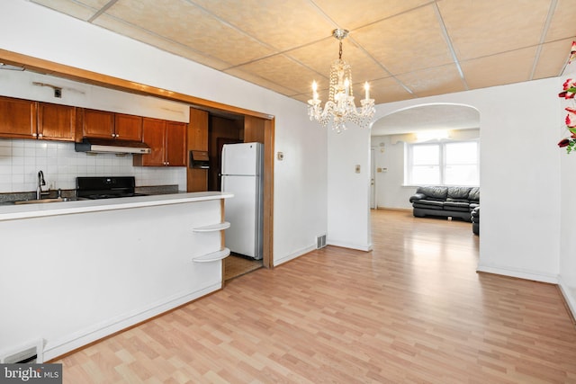 kitchen featuring under cabinet range hood, black range, a sink, freestanding refrigerator, and arched walkways