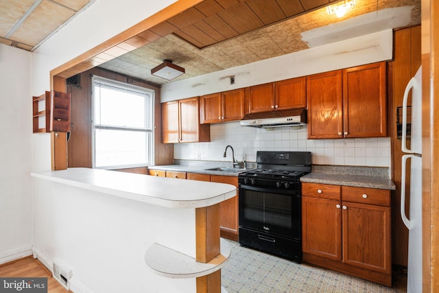 kitchen with freestanding refrigerator, a sink, decorative backsplash, black gas range, and under cabinet range hood