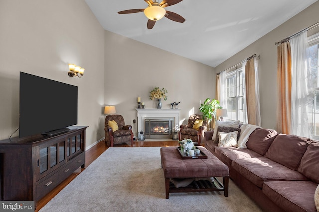 living area featuring a glass covered fireplace, lofted ceiling, wood finished floors, and ceiling fan