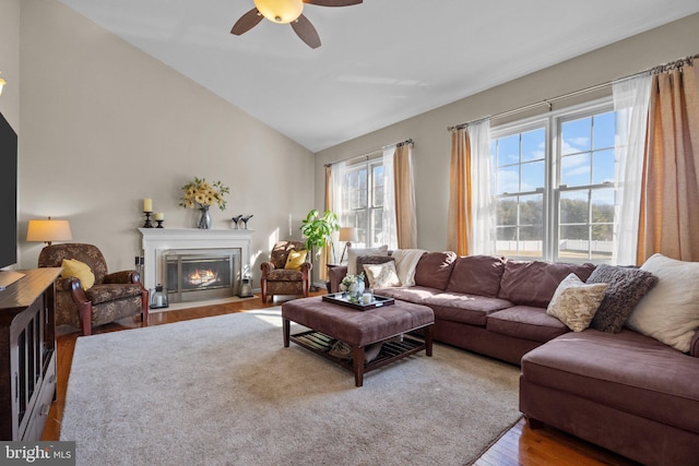 living room with lofted ceiling, a fireplace with flush hearth, wood finished floors, and ceiling fan