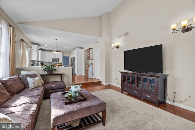 living room with visible vents, baseboards, an inviting chandelier, wood finished floors, and high vaulted ceiling